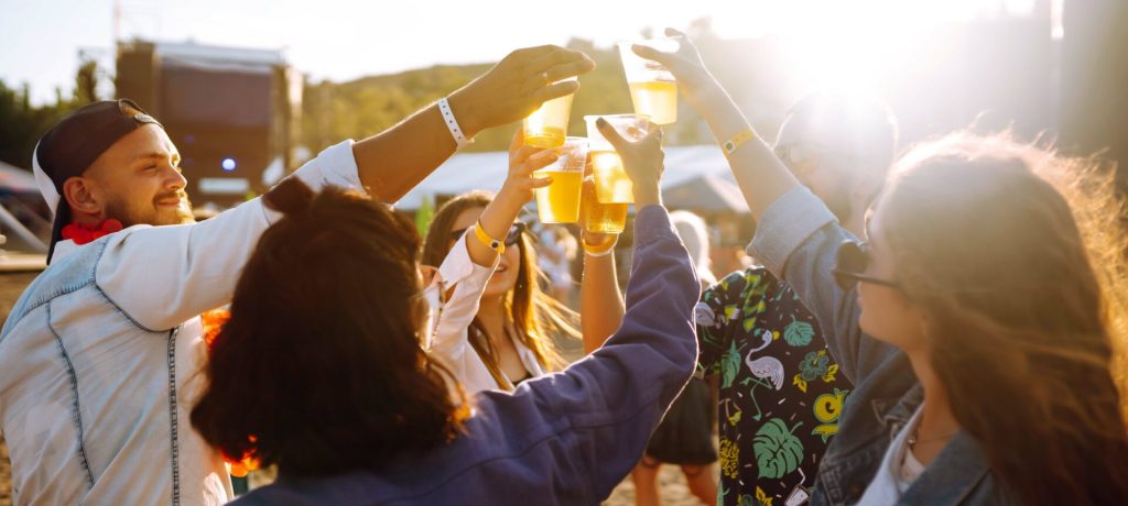 Young happy friends drinking beer and having fun at music festival together. Friendship.