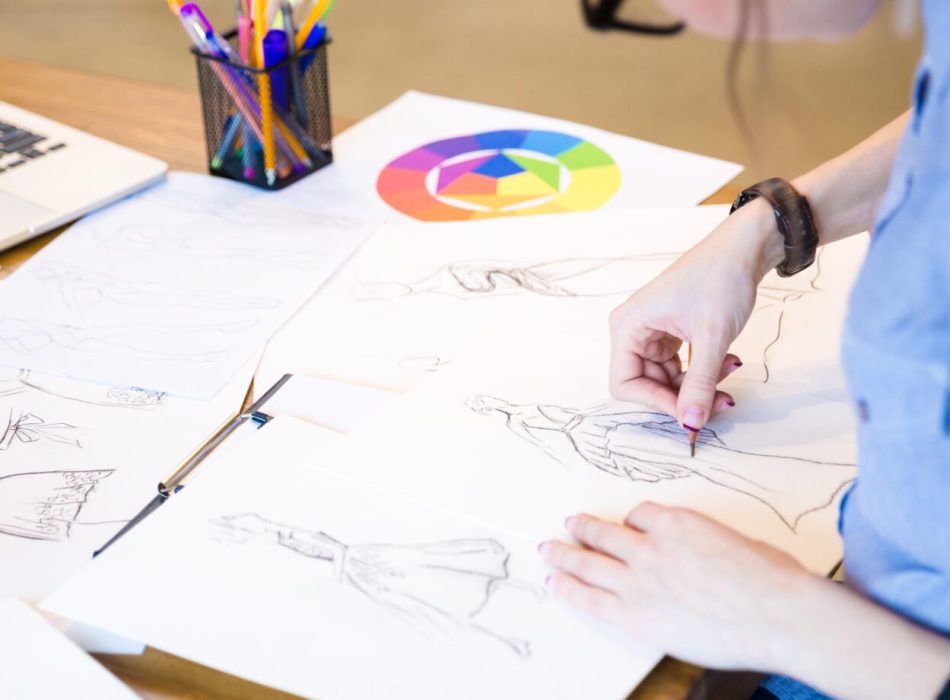 Closeup of creative young woman fashion designer in glasses sitting and drawing sketches at the table