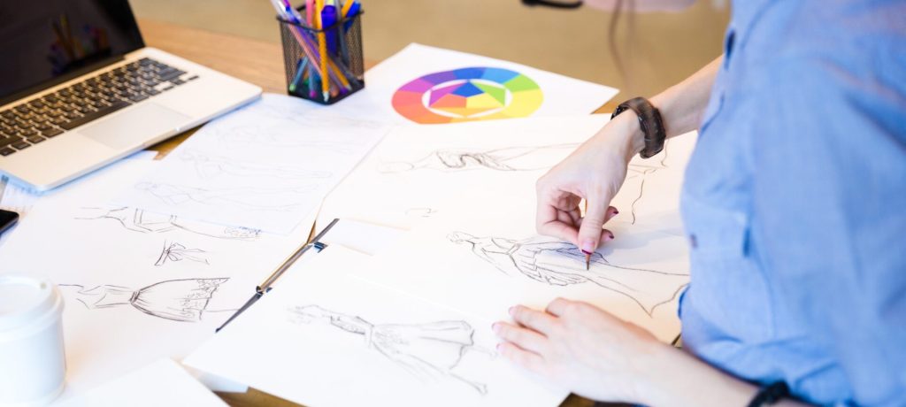 Closeup of creative young woman fashion designer in glasses sitting and drawing sketches at the table