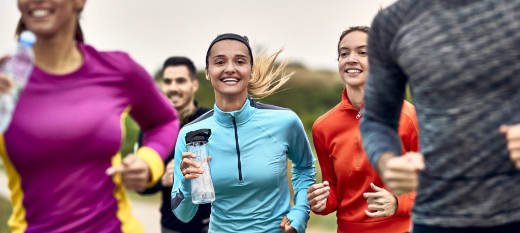 Young happy athletic women jogging with group of people in nature.