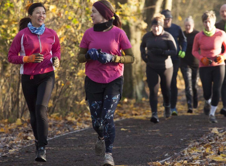 Group of adults jogging together on a leaf-strewn path in an autumn setting.