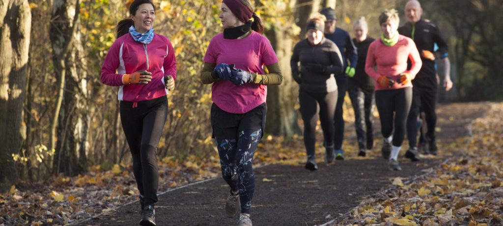 Group of adults jogging together on a leaf-strewn path in an autumn setting.