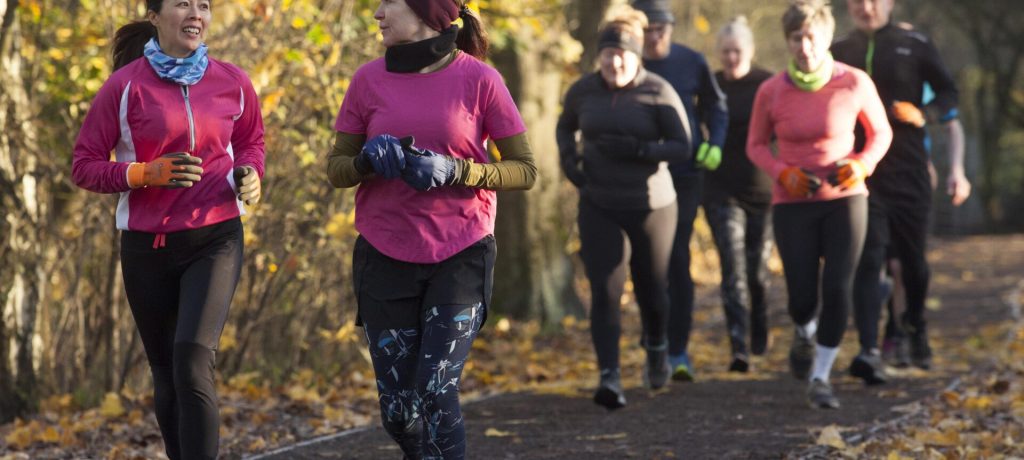 Group of adults jogging together on a leaf-strewn path in an autumn setting.