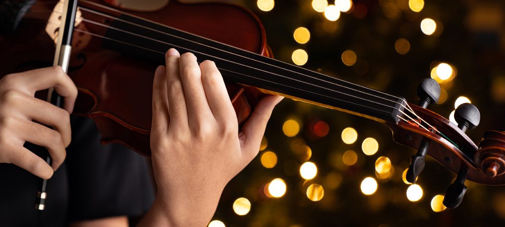 Teen girl performing holiday violin tunes in black formal wear on christmas background